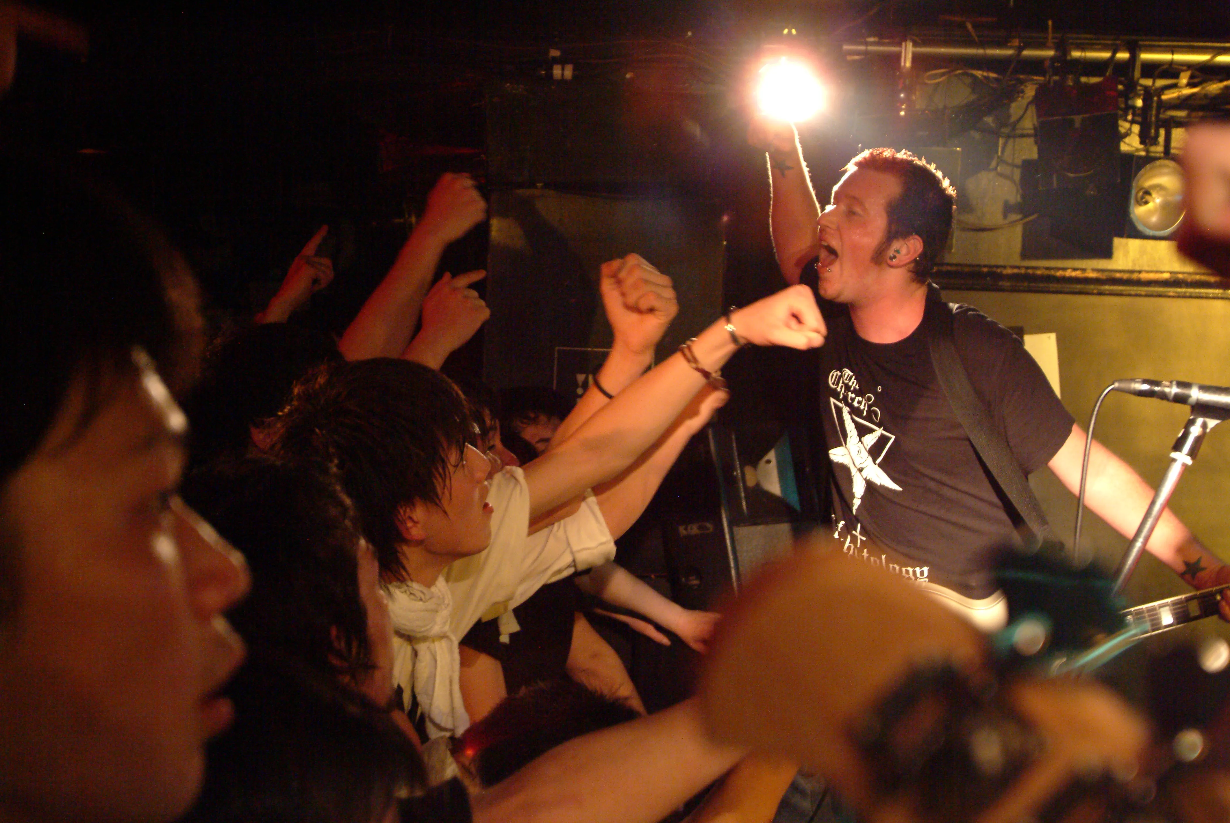 SecondShot guitarist shouting under a bright stage light with fans pumping their fists in front