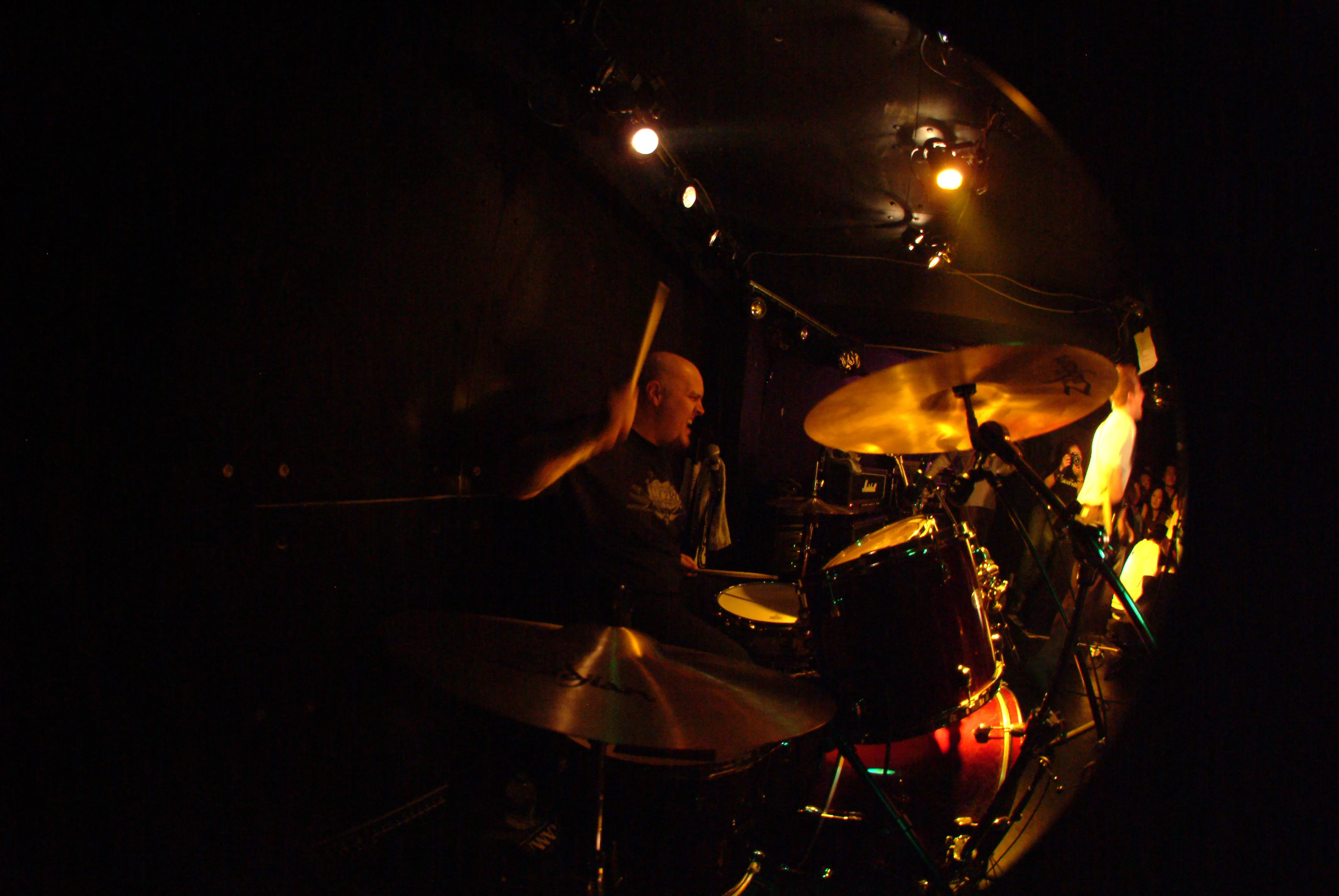 Fisheye shot of the SecondShot drummer mid-hit on a dark stage