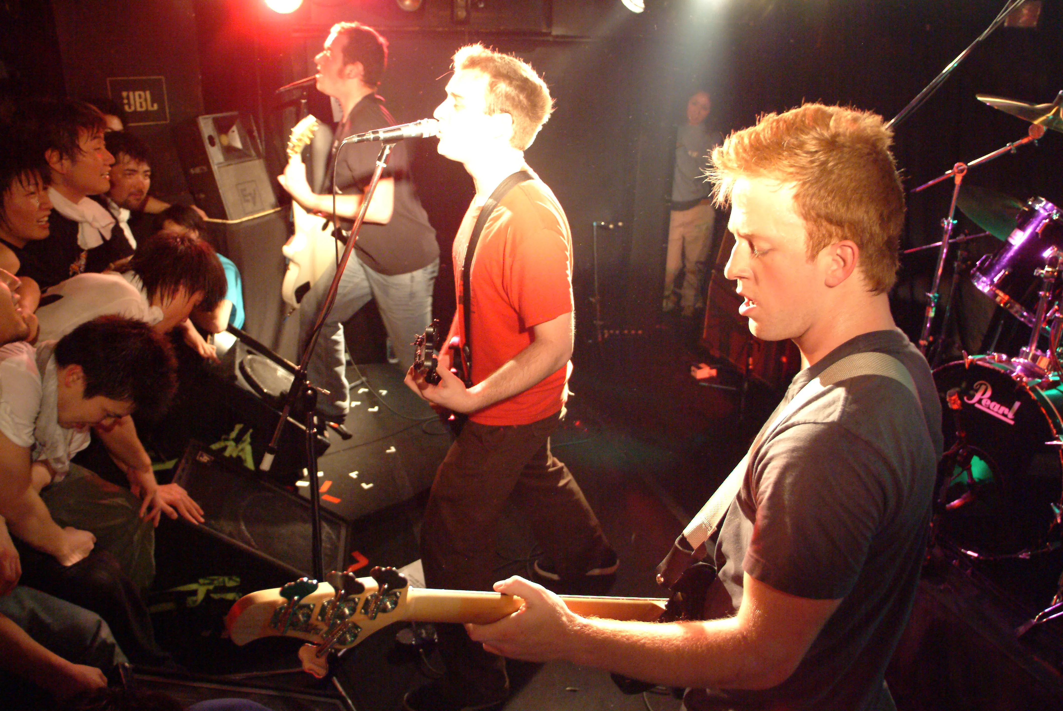 Three SecondShot members playing on a packed small stage with fans leaning against the stage edge