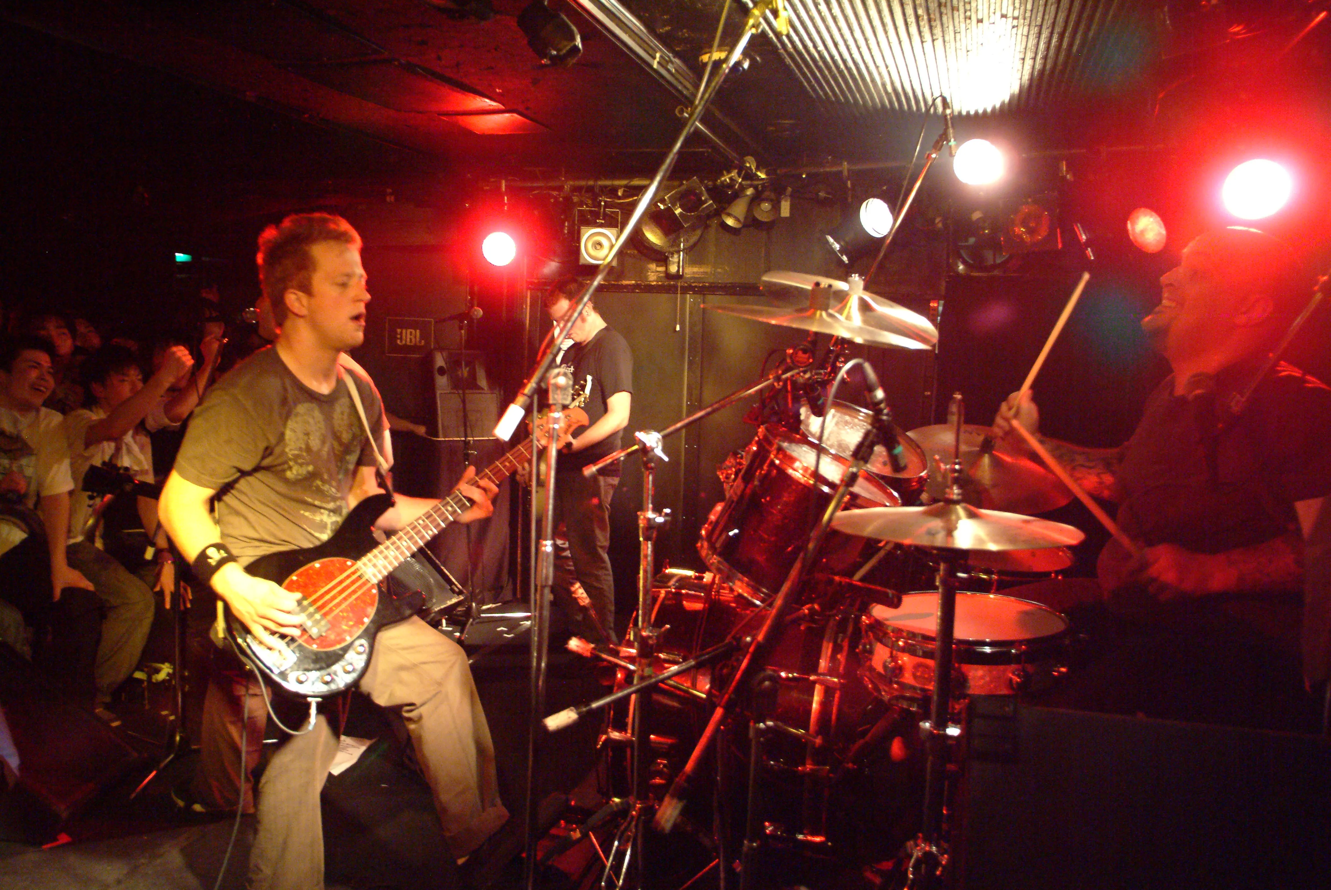 SecondShot bassist and guitarist playing while the drummer grins behind the kit and the crowd cheers