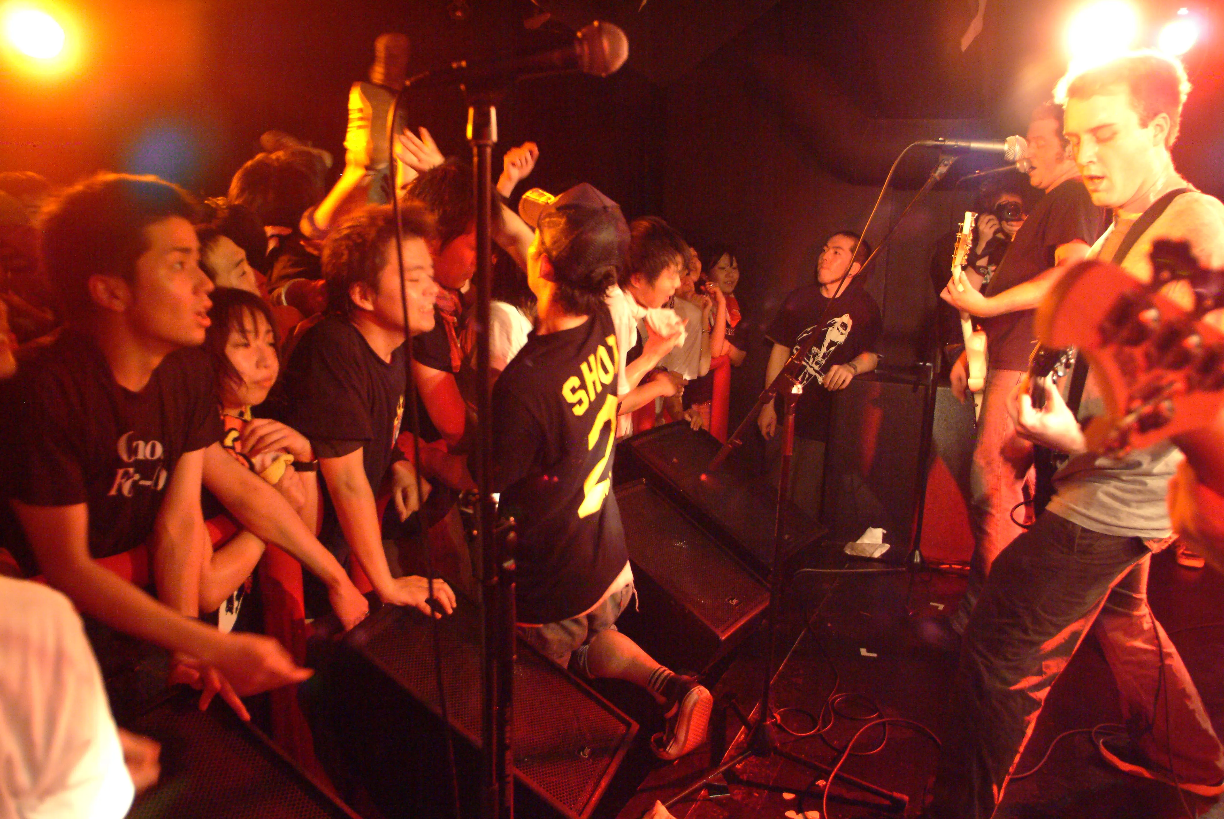 Fans packed against the barricade, hands reaching for the mic, with the SecondShot guitarist at right