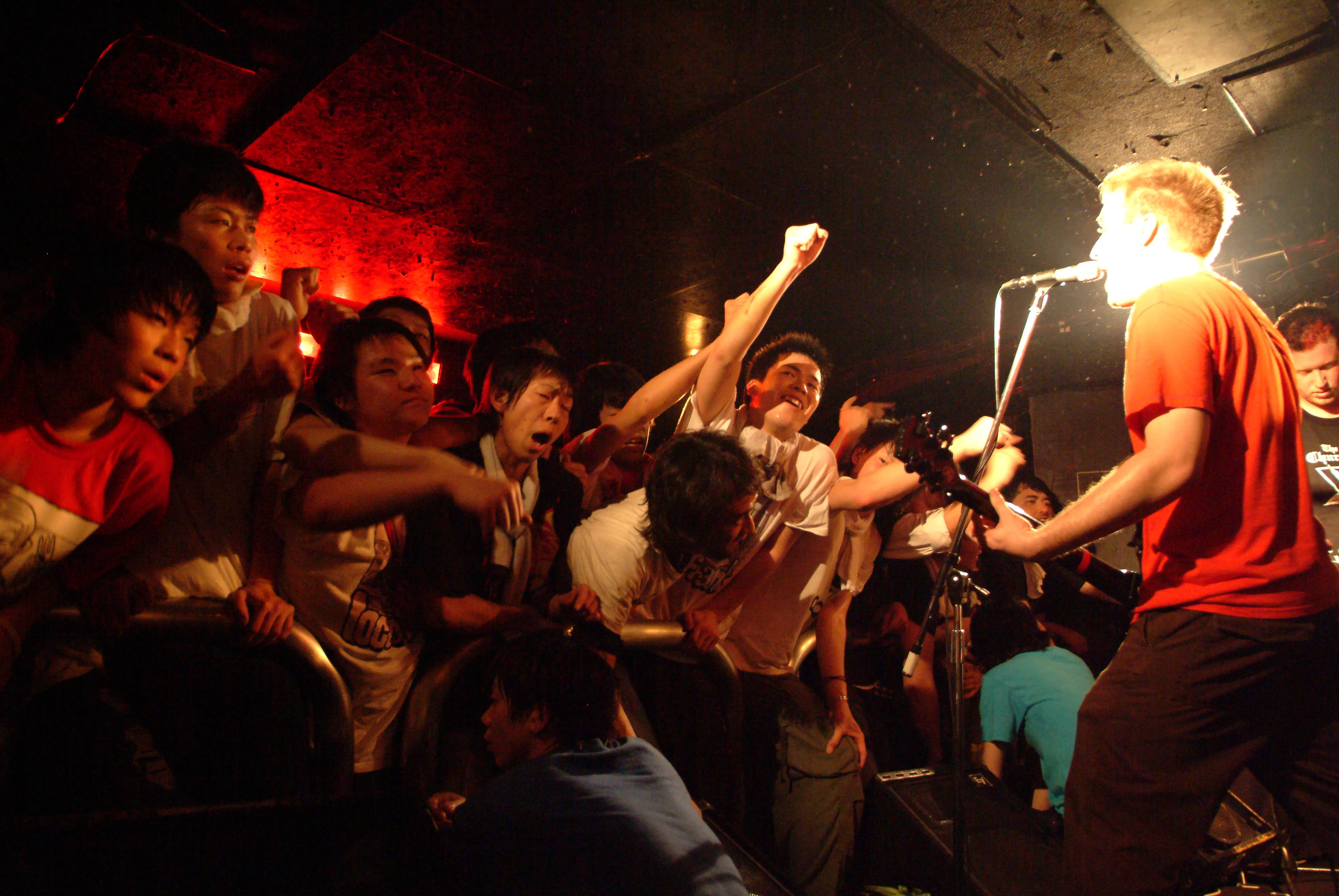 SecondShot guitarist in a red shirt singing to a crowd with fists raised at the barricade