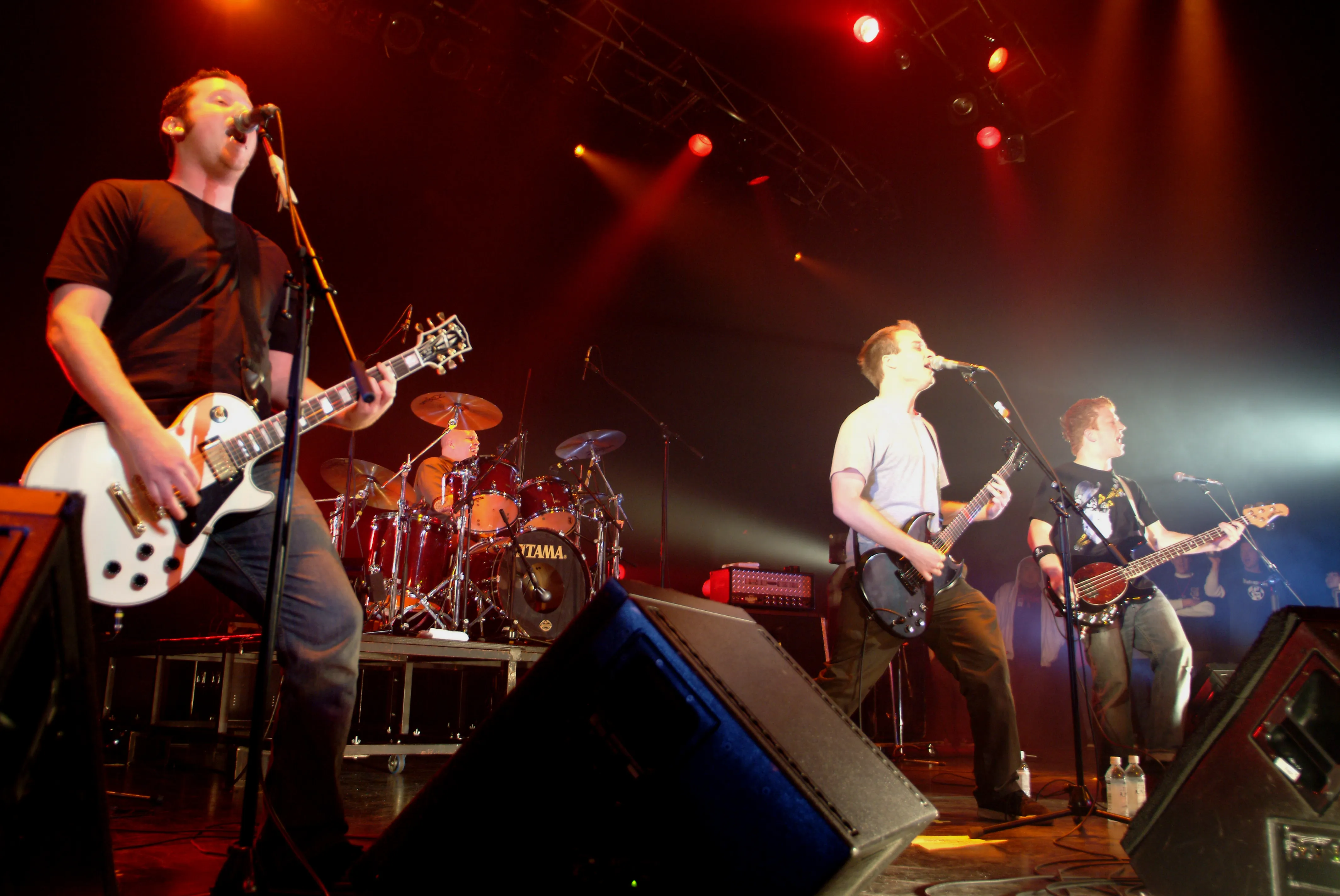 SecondShot playing a big stage under red lights, guitarist and bassist singing into mics